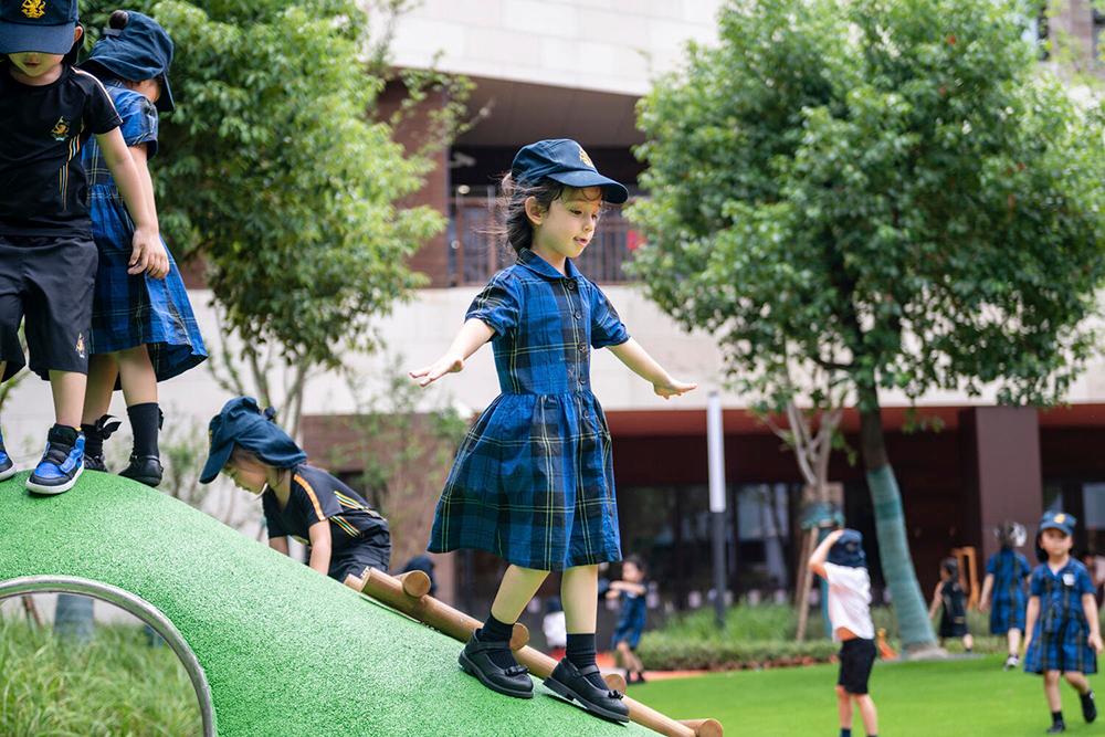 A young girl in uniform walks down a grassy slope in an open play area at Hiba Academy Bay Area, a private international preschool in San Francisco Bay Area offering Early Years bilingual curriculum.