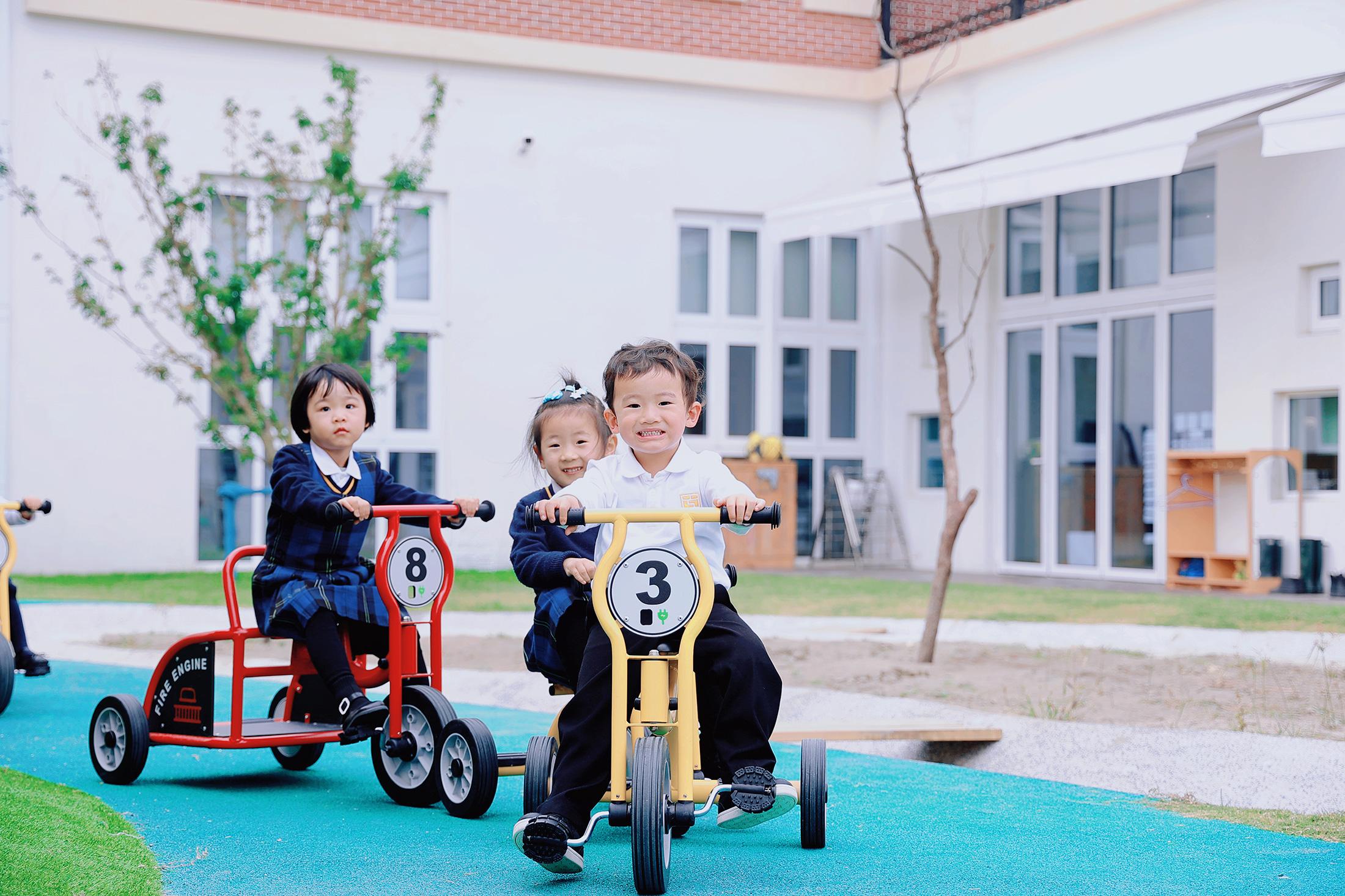 International preschool students riding modified bikes in the outdoor learning area of Hiba Academy Bay Area, a private preschool in San Francisco Bay Area with an Early Years curriculum encouraging holistic development of pre-kindergarten students.