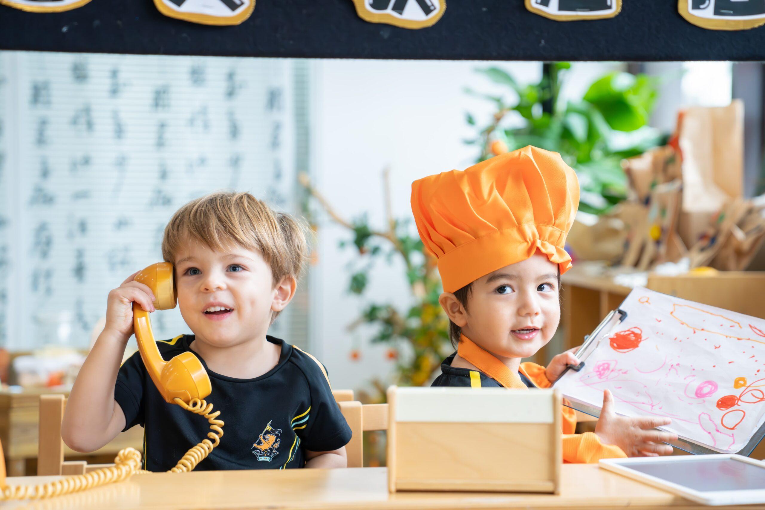 Two pre-kindergarten students role-playing as a waiter and chef taking orders on the phone as part of the bilingual Early Years curriculum at Hiba Academy Bay Area, a private international preschool in San Francisco Bay Area.
